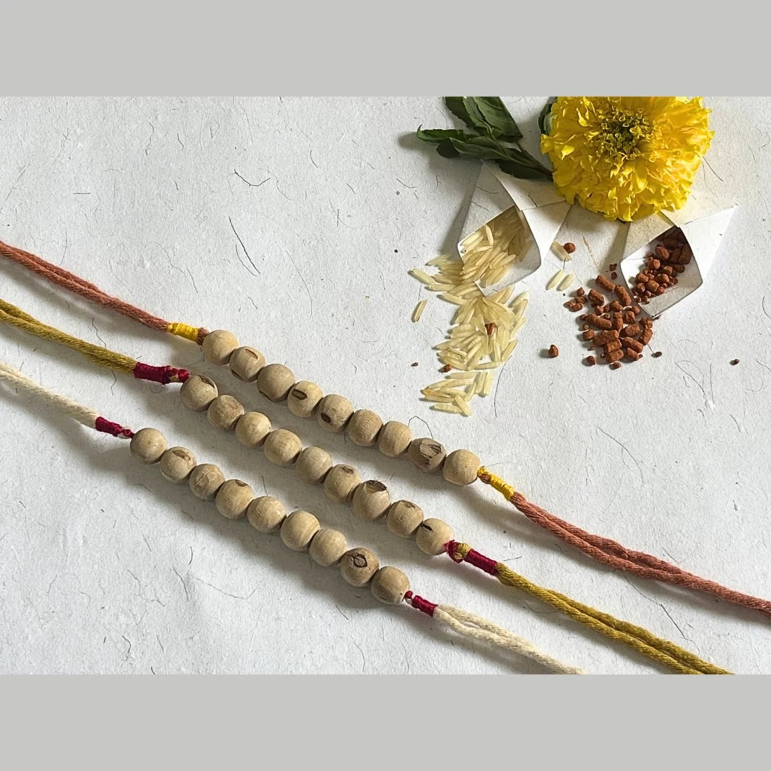 Eco-friendly Tulsi bead rakhi in Brick Red and Yellow and Natural White. Natural dyed organic cotton threads. Cotton potli packaging. Handmade in India.