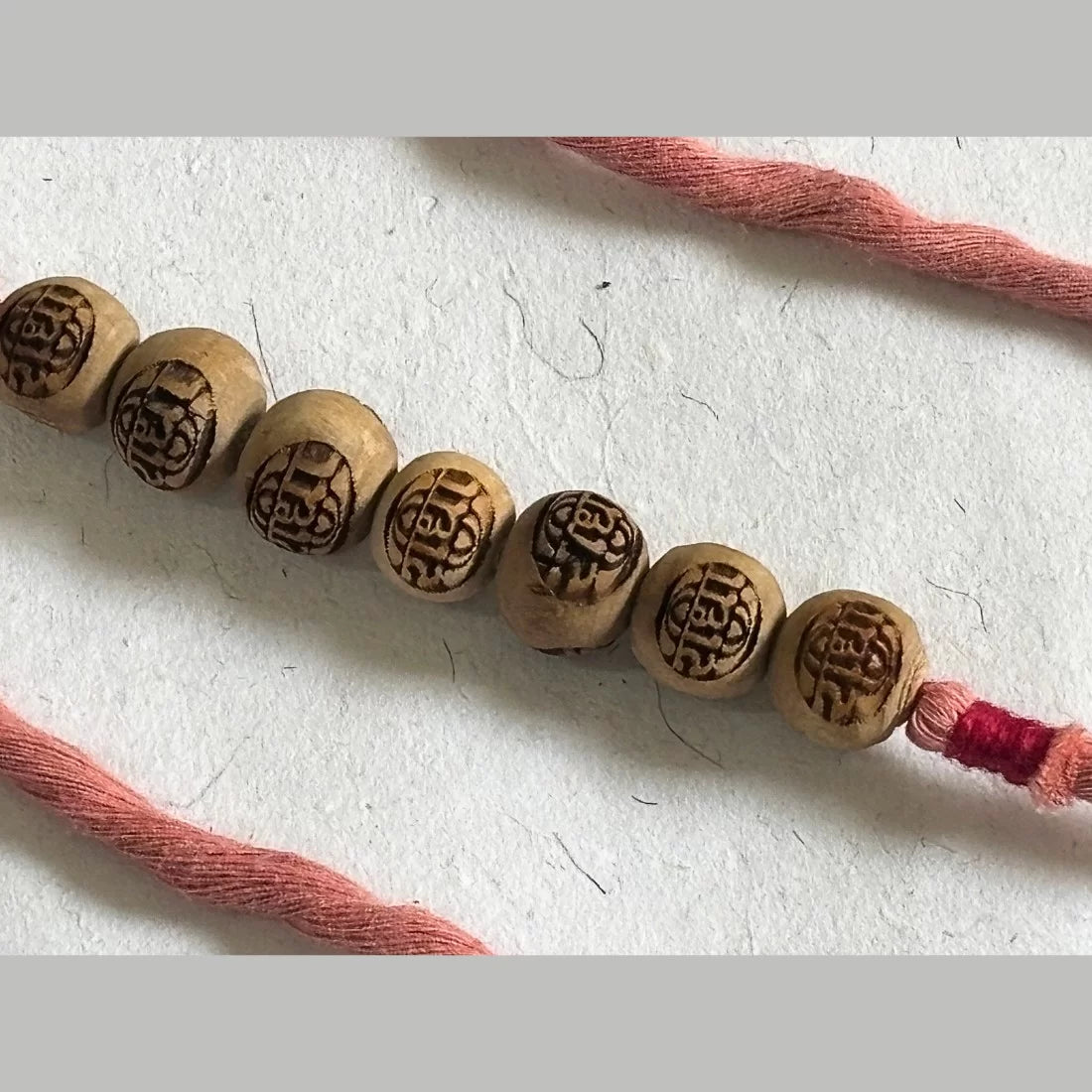 Eco-friendly Radha carved Tulsi bead rakhi in Dusty Rose Pink and Natural White. Handmade by women artisans. Cotton potli packaging. Made in India.