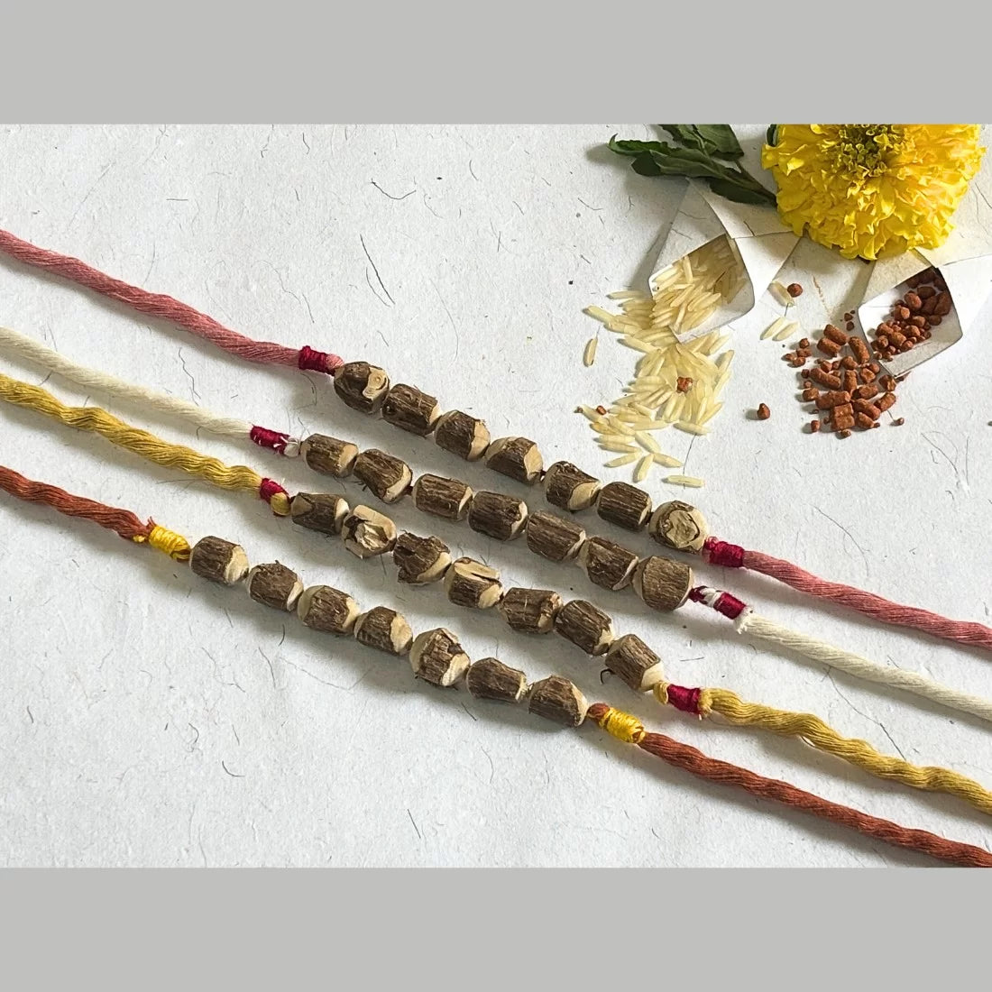 Eco-friendly Tulsi bead rakhi in Dusty Rose Pink and Yellow and White and Brick Red. Natural dyed organic cotton. Cotton potli packaging. Handmade in India.
